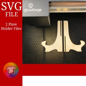 May include: SVG FILE 2 Plate Holder Files. A close-up of two wooden plate holders being cut by a Glowforge laser cutter. The holders are in the shape of a letter J with a curved top.