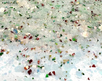 May include: Close-up of a white, glittery surface with red, green, and gold glitter scattered throughout.