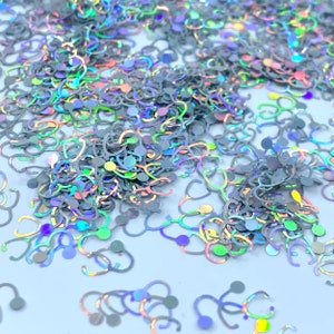 May include: A pile of iridescent holographic glitter shaped like stethoscopes. The glitter is a mix of silver, blue, green, and pink.