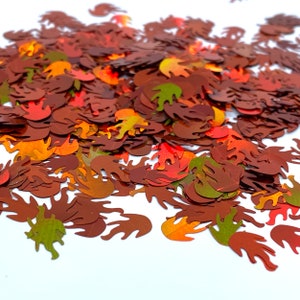 May include: A pile of colorful fall leaf shaped confetti in shades of red, orange, yellow, and green. The confetti is scattered on a white background.