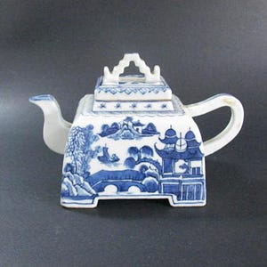 May include: A square blue and white porcelain teapot with a lid and a handle. The teapot is decorated with a Chinese landscape scene.