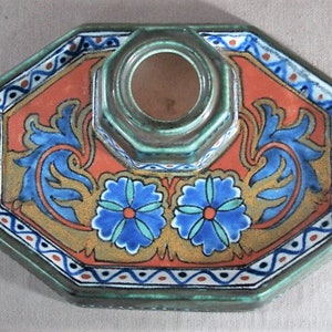 May include: An octagonal ceramic inkwell with a green, orange, blue, and white floral design. The inkwell has a separate well for ink and a raised, octagonal base.