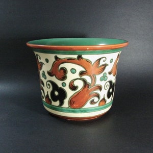 May include: A ceramic planter with a white background and a green, orange, and black floral design.