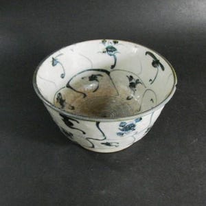 May include: A white ceramic bowl with blue and black floral designs. The bowl has a slightly rounded shape and a wide rim.
