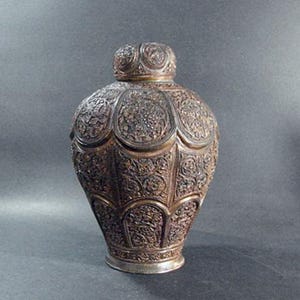 May include: An ornate, silver-colored metal vase with intricate floral patterns and a rounded, bulbous shape.