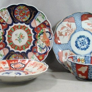 May include: Three Japanese porcelain plates with intricate floral and geometric designs in shades of blue, red, and white. The plates have scalloped edges and are decorated with gold accents.