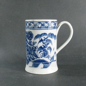 May include: White ceramic mug with a blue and white floral and dragon design. The mug has a curved handle and a flared base. The top of the mug features a blue geometric pattern. The mug is approximately 4 inches tall.