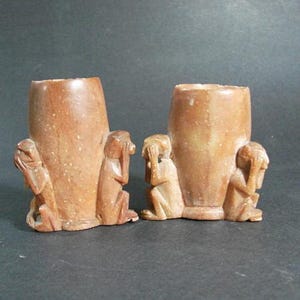 May include: Two brown stone cups with three monkeys carved on each side. The monkeys are covering their eyes, ears, and mouths.
