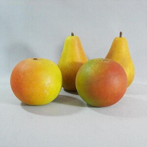 May include: Four fruit models, including two yellow pears and two round fruits, one yellow and one orange with red highlights. The fruits are arranged on a white surface.