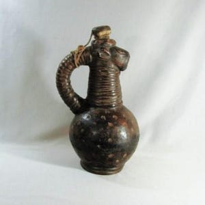 May include: A brown ceramic pitcher with a textured surface and a unique animal-shaped spout. The pitcher has a dark brown color and a speckled pattern.