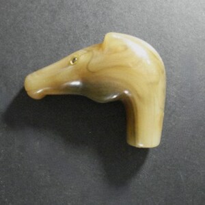 May include: A beige and brown carved cane handle shaped like a horse's head with a gold eye.