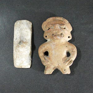 May include: Two small, ancient-looking clay figurines. One is a rectangular, off-white shape. The other is a tan-colored figure with a human-like form, featuring a head, arms, and legs, with holes in the body.