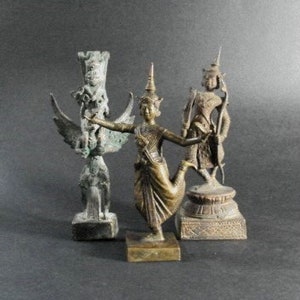 May include: Three bronze statues of figures from Southeast Asian mythology. The statues are on small wooden bases. The statue on the left is a winged figure with a crown. The statue in the center is a female figure with a crown and a raised leg. The statue on the right is a female figure with a crown and a raised arm holding a weapon.