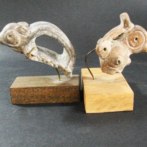 May include: Two small ceramic sculptures on wooden bases. The sculptures are abstract and feature a brown and white color scheme.