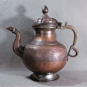 May include: An antique copper teapot with an ornate engraved design. The teapot has a lid with a finial and a handle with a decorative end. The teapot is on a gray background.