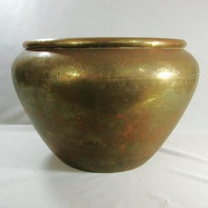 May include: A large, round, hammered brass planter with a slightly flared rim. The planter has a warm, golden color and a slightly distressed finish.