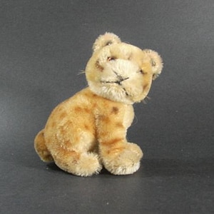 May include: A vintage plush toy lion cub in a seated position. The cub has a tan body with darker brown spots and a cream-colored face. It has small, round ears and stitched facial features.