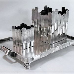 May include: Silver cigarette holder with a tray and two compartments. The compartments are made of vertical silver bars.