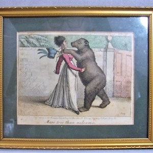 May include: An antique print in a gold frame depicts a woman being attacked by a bear. The woman is wearing a white dress and a red jacket. The bear is brown and has its claws out. The print is titled "More true than welcome."