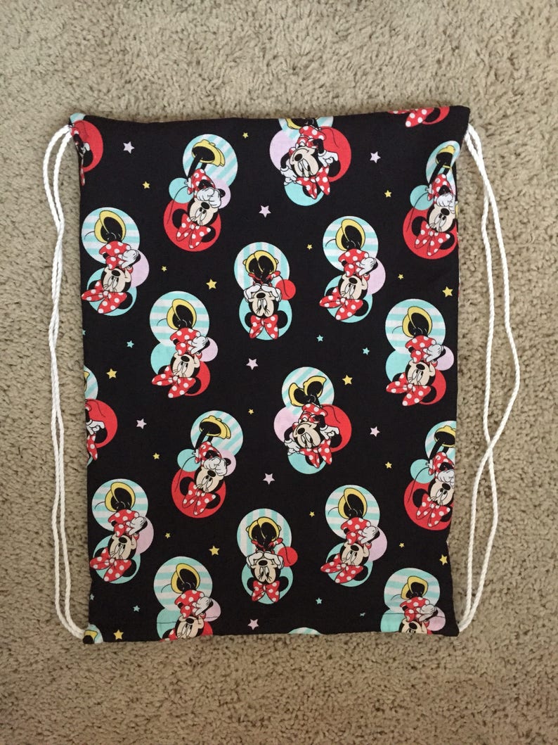 K&ouml;nnte beinhalten: Schwarze Kordelzugtasche mit einem sich wiederholenden Muster von Minnie Mouse in Rot, Wei&szlig; und Gelb auf schwarzem Hintergrund. Die Tasche hat wei&szlig;e Kordeln.