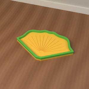Pode incluir: Uma bandeja em forma de leque com um interior amarelo brilhante apresentando linhas radiantes em relevo e uma borda verde elevada. O objeto tem uma base plana e uma silhueta geométrica distinta, exibindo um contraste entre as cores amarela e verde.