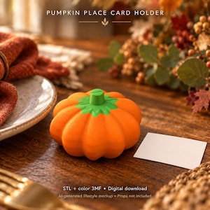 May include: A bright orange pumpkin-shaped place card holder with a green stem and a slit on top for holding cards. The object features a ribbed texture and is designed for table settings. The text PUMPKIN PLACE CARD HOLDER is visible.