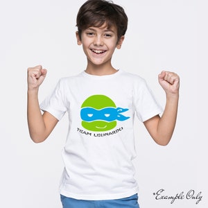 May include: White t-shirt with a green, blue, and black cartoon ninja turtle head graphic. The text "TEAM LEONARDO" is printed below the graphic.