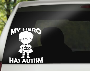 May include: White vinyl car sticker with a cartoon illustration of a superhero child holding a puzzle piece. The text reads "My Hero Has Autism".