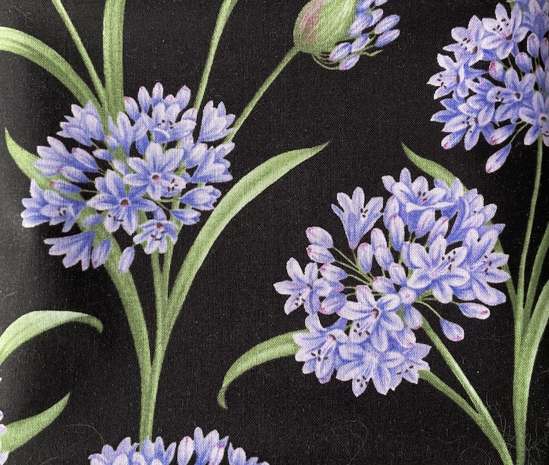 May include: A black fabric featuring a repeating pattern of light purple agapanthus flower clusters with green stems and leaves. The floral design displays multiple spherical blooms in various stages of opening against a solid black background.