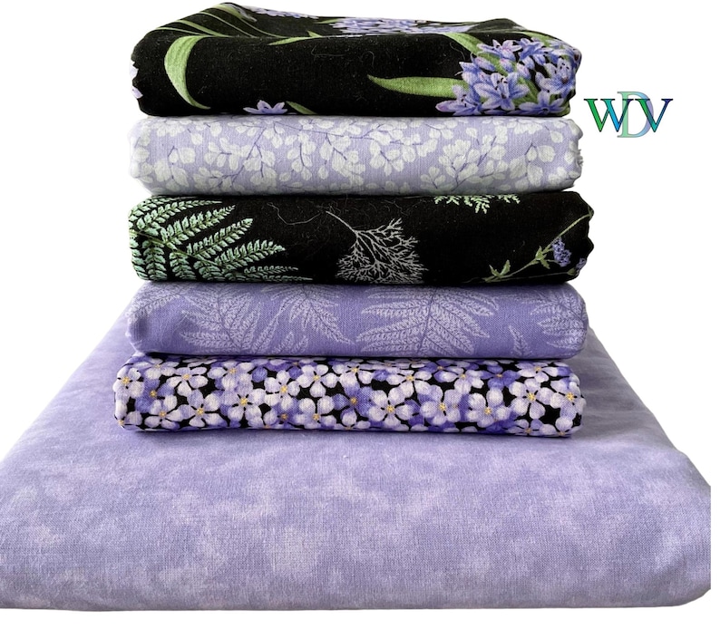 May include: A stack of six folded fabric pieces featuring various floral and botanical patterns in shades of purple, black, and white. The top piece is black with purple flowers, followed by light purple with white leaves, black with green ferns, light purple with fern patterns, purple flowers on black, and a solid light purple base.