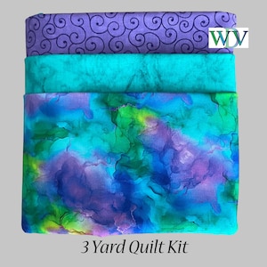 May include: A stack of three fabric pieces in shades of purple, teal, and blue. The top fabric has a swirling pattern, the middle is solid teal, and the bottom has a watercolor-like design. The text "3 Yard Quilt Kit" is at the bottom.