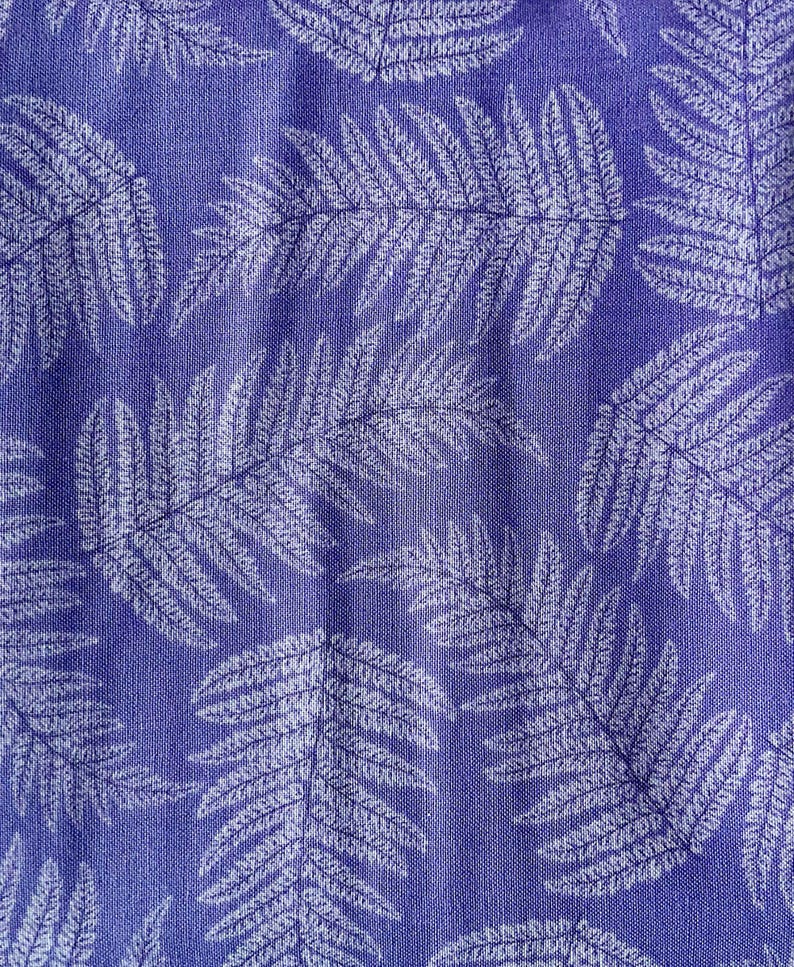 May include: A fabric textile featuring a repeating pattern of white fern leaves printed on a solid purple background. The material displays a visible woven texture throughout, with the botanical leaf shapes oriented in various directions across the surface.