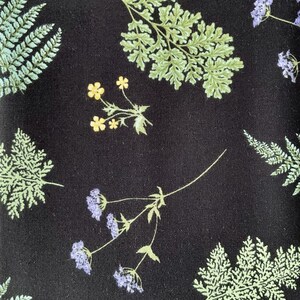 May include: A black fabric featuring a botanical print of light green fern fronds, small yellow flowers, and clusters of light purple blossoms. The pattern is distributed across the dark background, showcasing detailed leaf textures and floral stems.