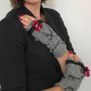 May include: A pair of gray fingerless gloves with black trim and red flower embellishments.