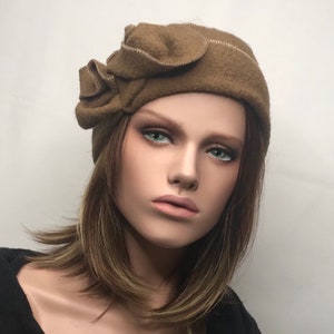 Peut inclure: Un chapeau en feutre marron avec un grand détail de fleur plissée sur le côté. Le chapeau est doux et a un design simple et élégant.