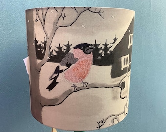 Lampshade with a wrap around design of a wintry scene with bullfinch and cosy cottage.