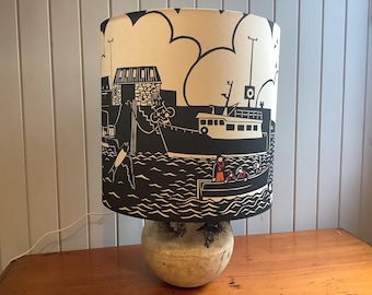 Lamp shade featuring a wrap around harbour design taken from a hand cut paper cut. Digitally printed onto a recycled/organic cotton.
