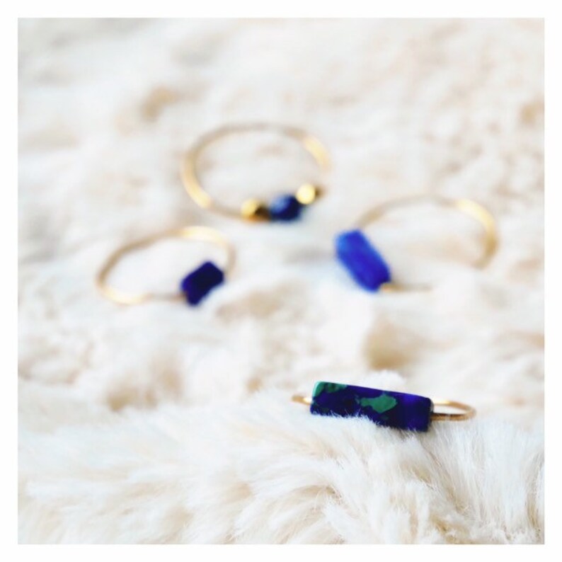Pu&ograve; includere: Quattro anelli sottili color oro con piccoli accenti di pietre blu e verdi. Un anello presenta una pietra rettangolare blu e verde, un altro una singola pietra blu, uno ha una pietra blu con due perline dorate e uno una pietra blu.