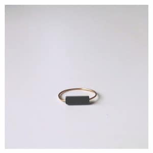 Pu&ograve; includere: Un sottile anello in metallo color oro caratterizzato da un unico inserto a barra rettangolare nera orizzontale centrato sulla fascia. L'anello presenta una finitura liscia e lucida e un design semplice che mette in risalto il contrasto tra oro e nero.