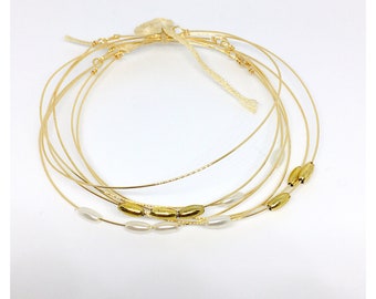 May include: A set of seven gold-toned wire bracelets with small white and gold beads. The bracelets are layered and have a delicate, minimalist style.