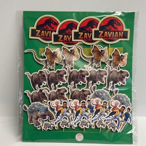 May include: A package of dinosaur-themed cake toppers. The toppers include various dinosaur species, characters, and logos with the text "Zavi" and "Zavian" in a red and black color scheme. The background is green.