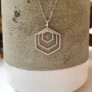 May include: A silver necklace with a geometric pendant made of three overlapping hexagons.