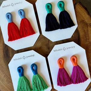May include: Four pairs of tassel earrings displayed on white cards with the text "inhabit jewelry". The earrings are in the colors red, green, blue, and pink.
