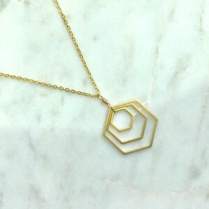 May include: A gold necklace with a geometric pendant featuring three concentric hexagons.