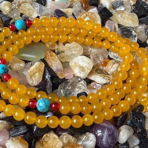 May include: A strand of yellow beads arranged in a circular pattern, featuring interspersed bright turquoise stone beads and small red accent beads. The yellow beads have a smooth, polished finish, while the turquoise beads display dark veining.