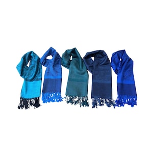 May include: Five blue scarves with fringe. The scarves vary in shades of blue, from light turquoise to deep navy. Each scarf has a patterned design and a contrasting border.