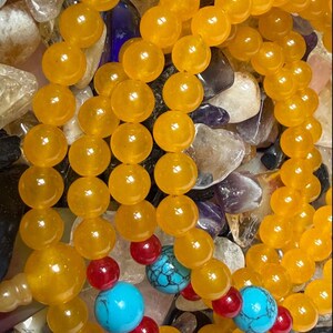 May include: A beaded necklace or bracelet featuring numerous smooth, round, translucent yellow beads. Interspersed among the yellow beads are smaller, vibrant red spherical beads and larger, round, bright turquoise beads with black veining.