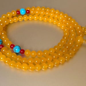 May include: A long strand of round, translucent yellow beads arranged in a circular pattern. The necklace features interspersed accents of bright turquoise blue stone beads and small, spherical red beads, finished with a knotted cord end.