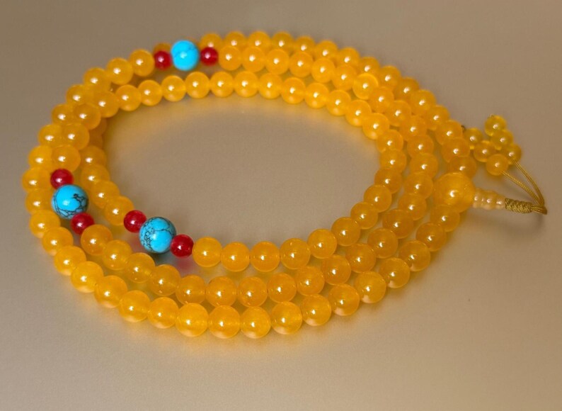 May include: A long strand of round, translucent yellow beads arranged in a circular pattern. The necklace features interspersed accents of bright turquoise blue stone beads and small, spherical red beads, finished with a knotted cord end.