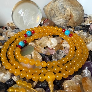 May include: A strand of yellow translucent beads arranged in a circular pattern, featuring interspersed bright turquoise round beads and small red accent beads. A larger yellow bead serves as a focal point at the bottom of the circular arrangement.